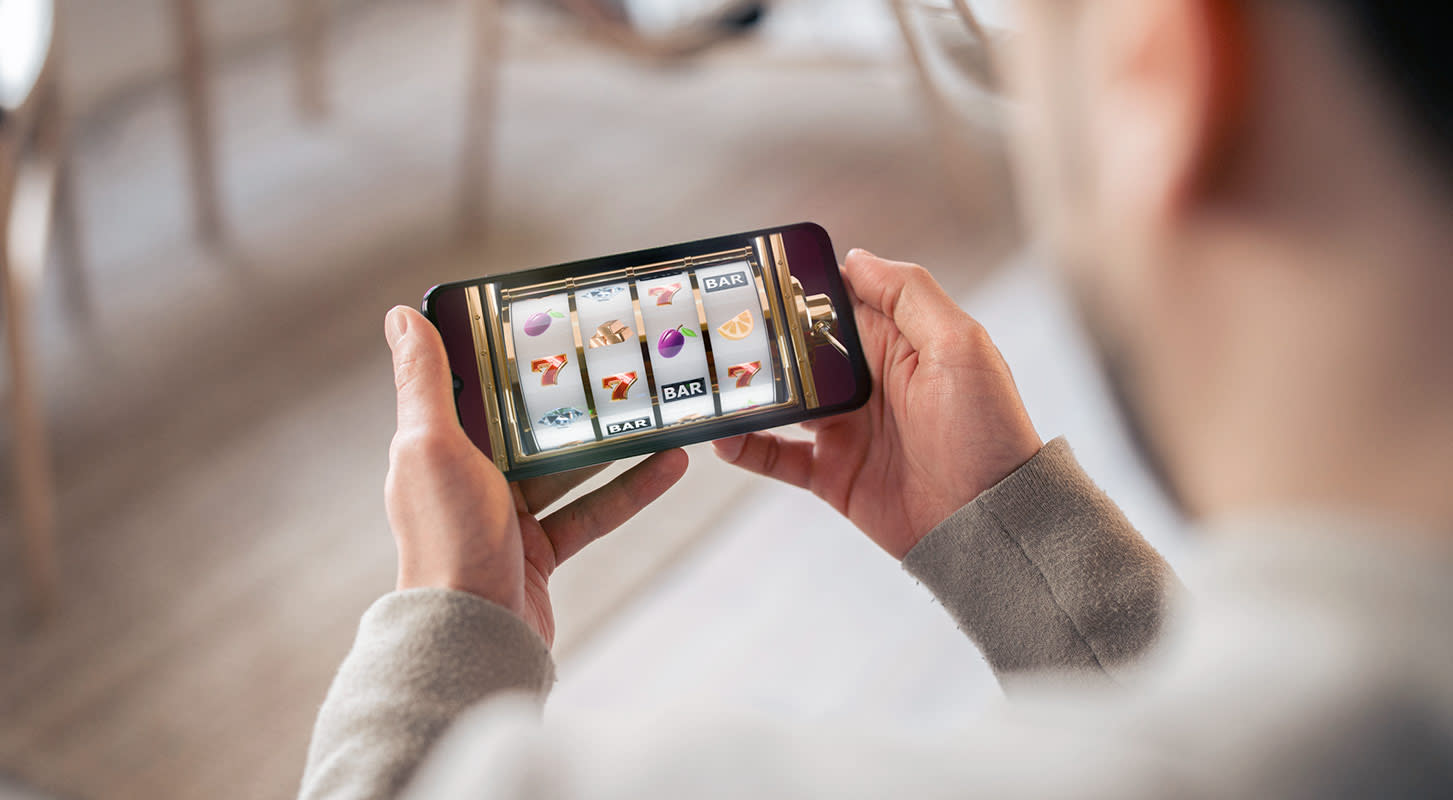 A man holding a smartphone displaying a colorful mobile game on the screen.